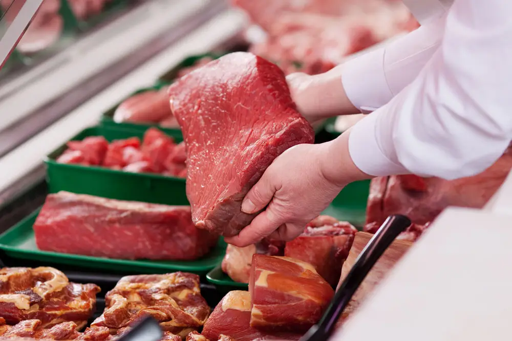 Boucher préparant une pièce de bœuf dans la vitrine de la Boucherie Vigne & Fils à Montélimar