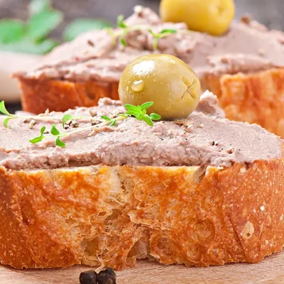 Tranche de pain grillée tartinée de pâté maison avec olive verte, préparation artisanale de la Boucherie Vigne & Fils à Montélimar